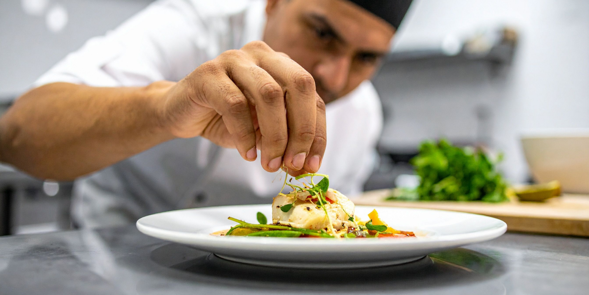Chef cuisinier ajoutant des herbes fraîches sur une assiette dressée
